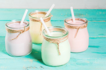 Small jars with a multi-colored smoothie or milkshake - pink cherry, purple berry, green and yellow orange. On a light blue wooden table copy space