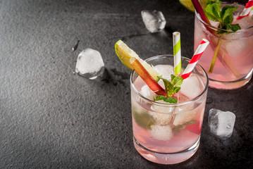 Summer refreshing drink, cocktail. Homemade organic mojito or lemonade with rhubarb, mint and lime. On a black concrete stone table, in glasses and a bottle. Copy space