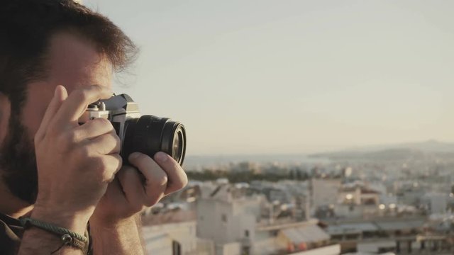 A young passionate photographer using a vintage film camera to photograph the city during sunset from a high angle