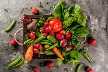 Market. Healthy vegan food. Fresh vegetables, berries, greens and fruits in wooden tray: spinach mint thyme strawberry carrots beets cucumbers radish green peas. On gray table. Copy space top view © ricka_kinamoto