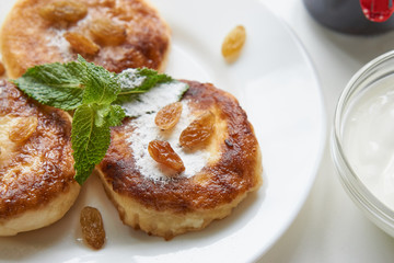 three pancakes on a white plate on white table covered with sugar powder, mint, raisins. low angle close up shot. isolated white on white