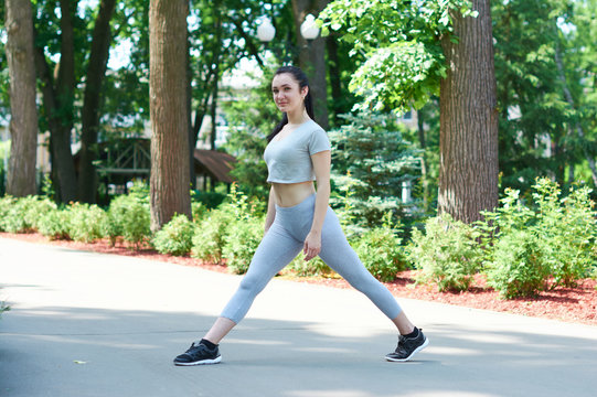 Beautiful brunette girl exercising in a green park. Training in nature. A healthy lifestyle. Sportswear. Happy girl.