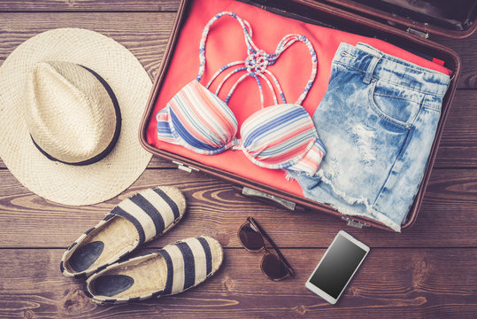 Open Suitcase With Summer Or Beach Clothes And Accessories On Wooden Table