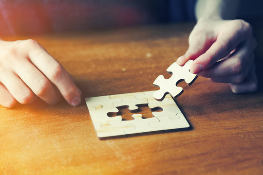 hands solving jigsaw puzzle with wooden pieces
