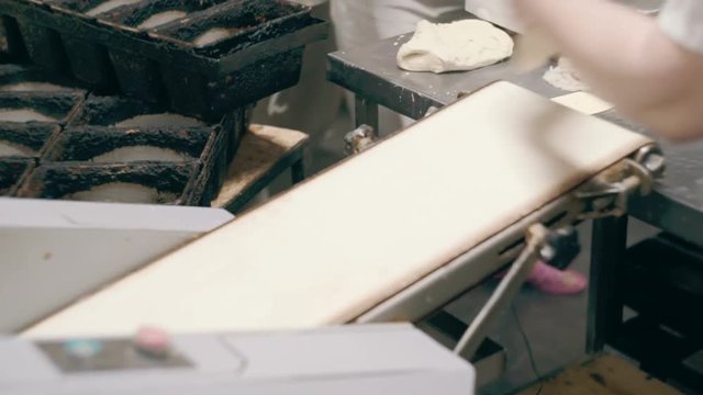 Woman takes the dough from the conveyor and puts it in the mold