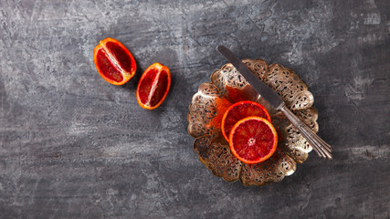 Blood Orange in a metal Plate with a knife on a dark Background.Vintage style.Food or Healthy diet concept.Vegetarian.Copy space for Text. selective focus.