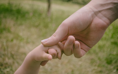 Children's fingers are held by the finger of an adult.