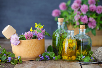 Bottles of tincture or infusion of healthy herbs, healing herbs and wooden mortar of flowers on rustic table. Herbal medicine.