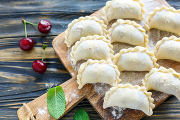 Traditional dumplings with cherries on a wooden board.