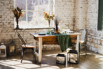 Coziness at home. Modern interior design. Beautiful vintage dining table with flowers, candles and laying near the window. Loft, botanic, rustic style. Table set for an event, party, date or wedding.