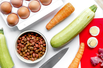 Bowl of dry dogfood, carrot, courgette and meat table background