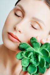 Portrait of a beautiful young brunette woman with green leaf in his hand in the studio, the concept of beauty and health