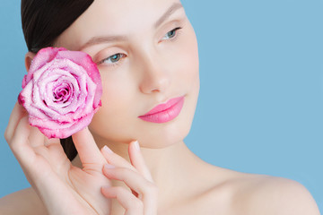Portrait of a beautiful brunette girl with a pink rose on a blue background