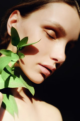 Portrait of a beautiful young brunette woman with green leaf in his hand in the studio, the concept of beauty and health