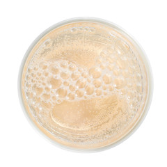 Cider close up, top view. Light yellow frothy drink with foam and bubbles in simple glass.