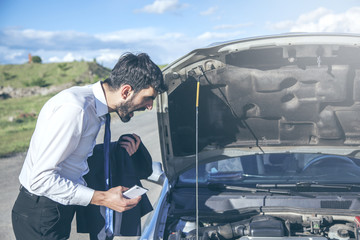 young businessman checking the broken car machine on the road