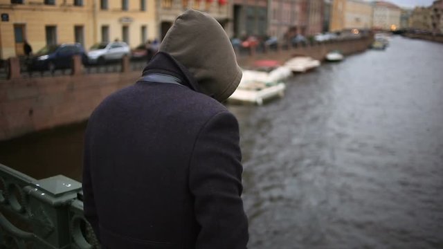 man in a coat stands on a bridge and looks down at the black water. She wants to commit suicide