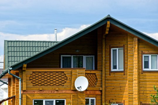 фасад коричневого деревянного дома с окнами и спутниковой антенной