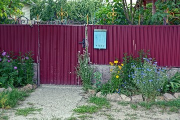 красный железный забор с почтовым ящиком с травой и цветами