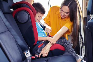 Gorgeous mom helping son to fasten seat belt
