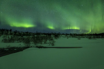 Northern lights above a water stream in a winter landscape.