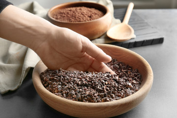 Human hand taking pile of cocoa nibs from wooden bowl