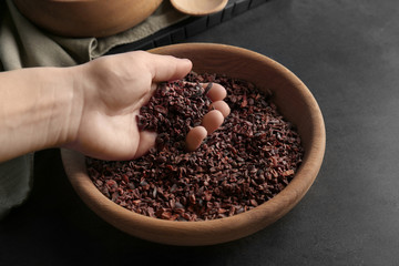 Human hand taking pile of cocoa nibs from wooden bowl