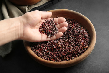 Human hand taking pile of cocoa nibs from wooden bowl