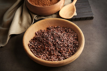 Cocoa nibs in wooden bowl on grey table