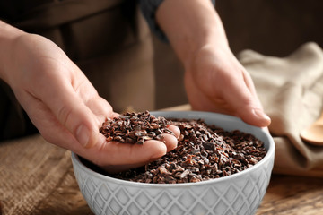 Person with cocoa nibs in hand over bowl on table