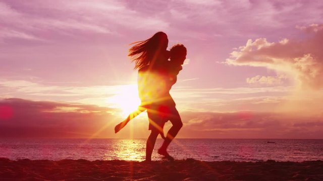 Couple piggybacking on beach having fun enjoying sunset on honeymoon summer travel vacation holiday. Happy joyful lovers playful together.
