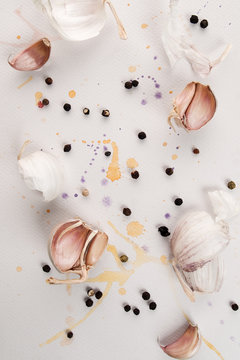 Garlic cloves and black spicy pepper lie on a white textured background with watercolor multicolored sprays.
