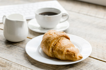 croissant and cup of coffee on office desk for business breakfast wooden background