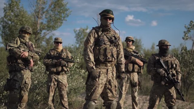 Group of soldiers in a camouflage and the hidden persons with weapon pose and look in the camera