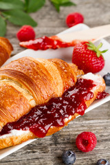 Closeup of tasty fresh appetizing croissants with fruit jam, cottage cheese and fruits on white plate. Breakfast.