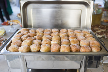 Donuts with icing sugar on baking pan heating in a wedding reception