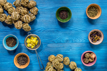 herbs in colorful bowls to make tea on blue table background top view