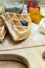 Waffles with berries,fruit and ice-cream in wood plate on table.