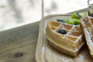 Waffles with berries,fruit and ice-cream in wood plate on table.