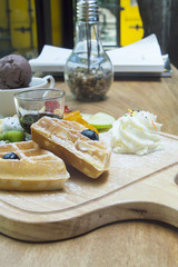 Waffles with berries,fruit and ice-cream in wood plate on table.