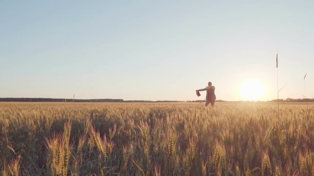 Successful businessman in a suit and with a leather briefcase, arms outstretched and simulating an airplane, runs through the wheat field towards the sun, slow motion