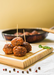 Meatballs in tomato sauce on a wooden board with toothpicks against white background