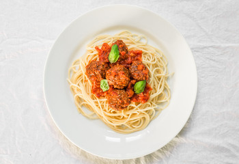 Spaghetti pasta with meatballs in tomato sauce and basil leaves against white background