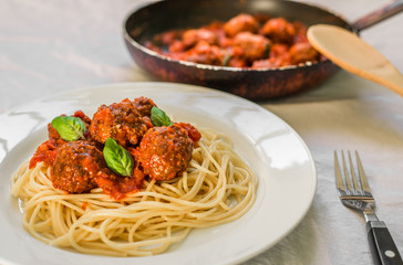 Spaghetti pasta with meatballs in tomato sauce and basil leaves against white background