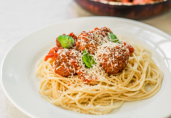 Spaghetti pasta with meatballs and cheese in tomato sauce and basil leaves against white background