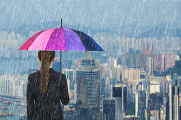 business woman holding multicolored umbrella with falling rain at city