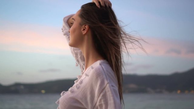 Closeup portrait of sensual woman in white linen dress posing on the sandy beach on tropical paradise island with beatiful summer sunset sky - video in slow motion