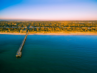 Aerial view of long wooden pier stretching into the ocean and coastal vegetation at sunset