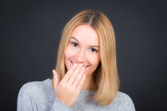 Nette blonde Frau hält beim Lächeln Hand vor den Mund