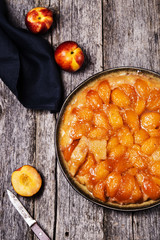 Tarte tatin upside down peach tart on vintage rustic wooden table. Summer baking. French cuisine. Selective focus. Toned image 